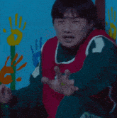 a man in a red and green vest with the number 12 on it is standing in front of a wall with handprints on it .