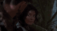a man and a woman are standing next to each other in the woods and looking at each other .