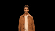 a man wearing a brown jacket and striped shirt smiles for the camera
