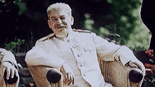 a man in a white uniform sits in a wicker chair smiling