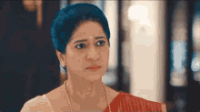 a woman in a red saree and pearls is looking at the camera .