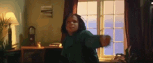 a woman in a green sweater is dancing in a living room with a window .
