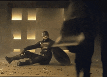 a man in a superhero costume is laying on the ground holding a shield