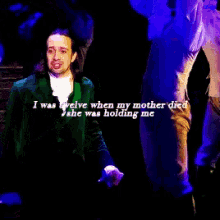 a man in a green jacket stands on a stage with the words " i was twelve when my mother died "