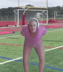 a woman in a pink shirt and headphones is standing on a field .