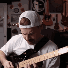 a man playing a guitar in front of a wall with guitars on it