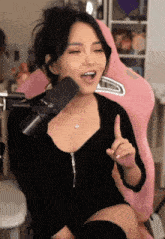 a woman in a black dress is sitting in front of a pink chair with a microphone .