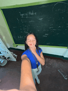a girl taking a selfie in front of a blackboard that says " types of media "