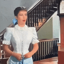 a woman in a white shirt and blue skirt is standing in front of a staircase