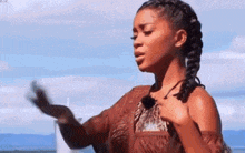 a woman in a brown dress is standing on a beach with her hands outstretched .