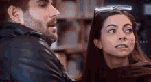 a man and a woman are looking at each other in a library . the woman is wearing glasses and a scarf .