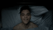 a shirtless man is laying in a bed and smiling