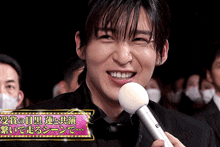 a man is smiling while holding a microphone in front of a sign that has chinese writing on it