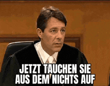 a man in a judge 's robe is sitting in front of a sign that says jetzt