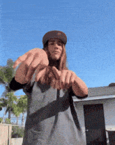 a man with long hair wearing a hat and a grey shirt is making a peace sign