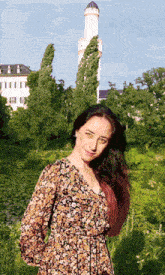 a woman in a floral dress stands in a field with a building in the background