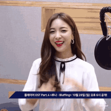 a woman in a white shirt stands in front of a microphone with a sign that says ost part 4 < buffing >