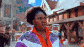 a woman in a purple and orange jacket is making a funny face while standing on a street .