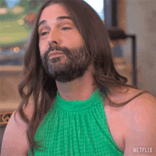a man with long hair and a beard is wearing a green dress and making a funny face .