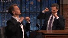 two men in suits and ties are sitting at a table with their fists in the air in front of a microphone .