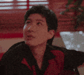 a man in a red and black shirt is sitting at a table looking up .
