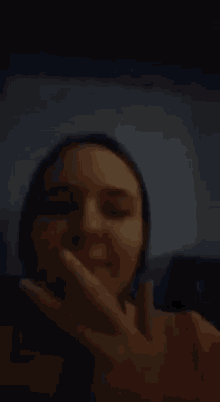 a woman is covering her mouth with her hand while looking at the camera .