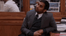 a man in a suit and tie is sitting at a desk with his hands on his hips .