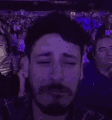 a man covering his face with his hand in a dark room with purple lights .