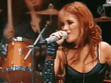 a woman singing into a microphone in front of a drum set