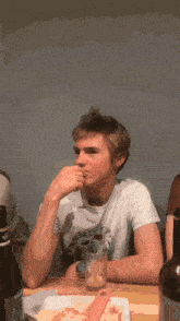 a young man sits at a table with a bottle of beer and a glass of beer