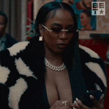 a woman wearing sunglasses and a fur coat looks at her cell phone