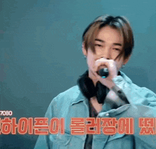 a young man is singing into a microphone while wearing headphones and a jacket .
