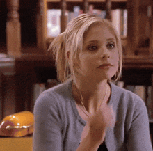 a woman in a blue sweater is sitting in front of a bookcase