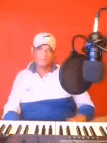 a man is playing a keyboard in front of a microphone while wearing a hat .