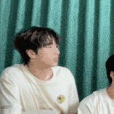 a man in a white t-shirt is sitting next to another man in a green room .