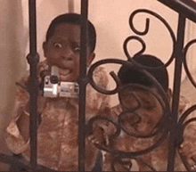 a boy is taking a picture of another boy behind a wrought iron fence .