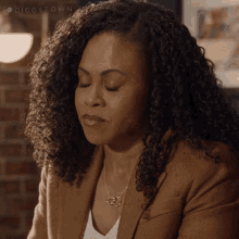 a woman with curly hair is wearing a brown jacket and a white shirt