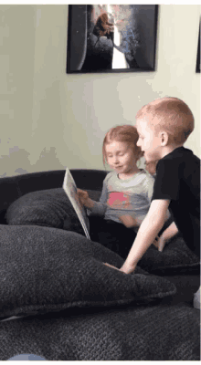 a boy and a girl sit on a couch looking at a book