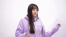 a young girl wearing a purple hoodie is standing in front of a white background .