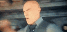 a bald man in a suit and tie is standing in front of a crowd .