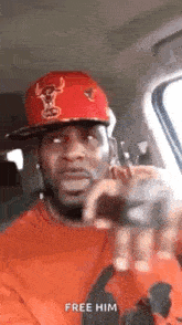 a man wearing a red hat and an orange shirt is sitting in a car talking on a cell phone .