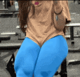 a woman wearing blue pants and a tan shirt is sitting on a bench in a gym
