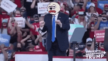 a man in a suit and tie is standing in front of a crowd at a trump rally .