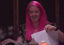a woman with pink hair holds a piece of paper in her hand