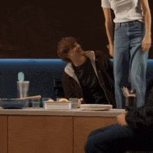 a woman in a white shirt is standing over a man in a kitchen