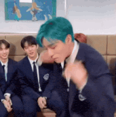 a man with blue hair is sitting on a couch next to two other men in suits and ties .