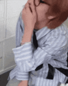 a man in a striped shirt and tie is covering his face with his hand .