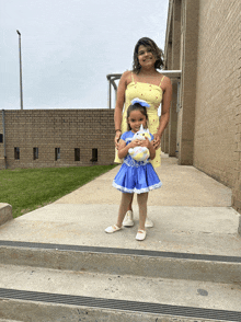 a little girl in a blue dress is holding a stuffed animal