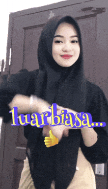 a woman wearing a hijab is giving a thumbs up with the words " luar biasa " above her
