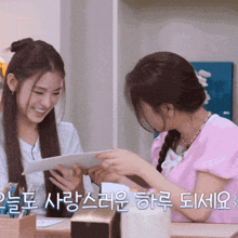 two girls are sitting at a table with korean writing on the bottom right